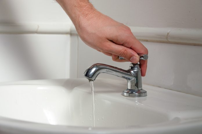 a white male hand turning off a sink faucet
