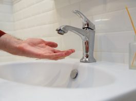 Man holding his hand under opened tap without water